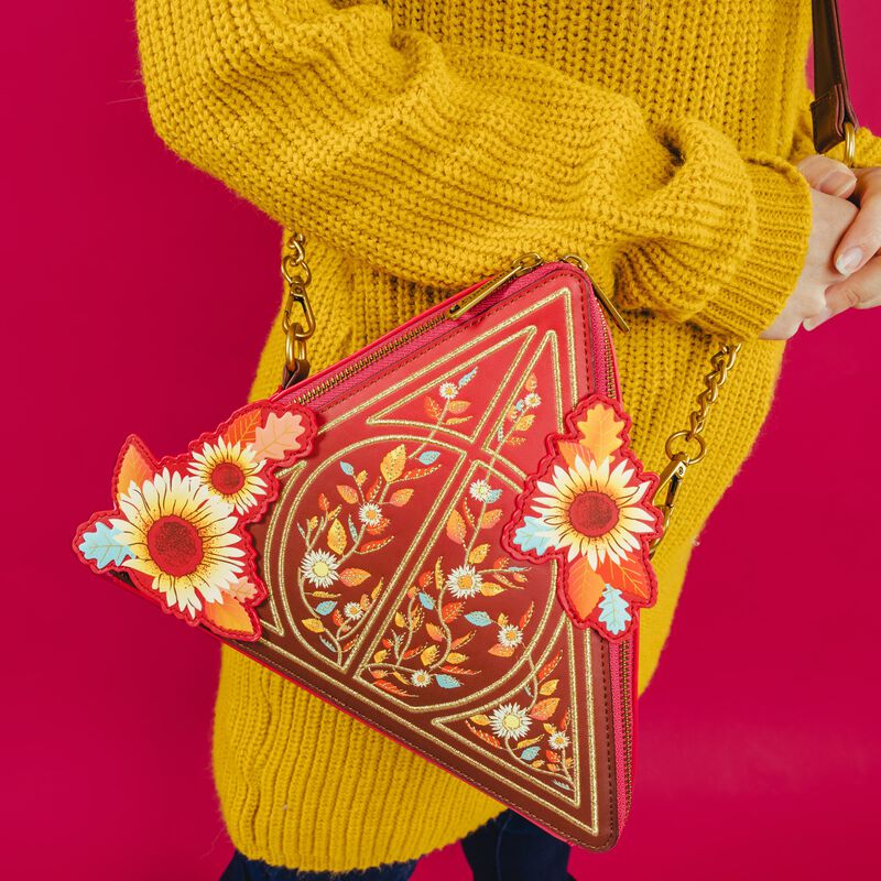 Image of a person wearing a yellow sweater and wearing our Deathly Hallows Fall Leaves Crossbody Bag against a red background